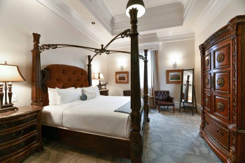 Luxurious bedroom featuring a four-poster bed, elegant furnishings, and warm lighting in a classic design.