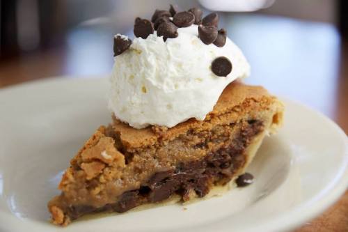A slice of cookie pie topped with whipped cream and chocolate chips on a white plate.