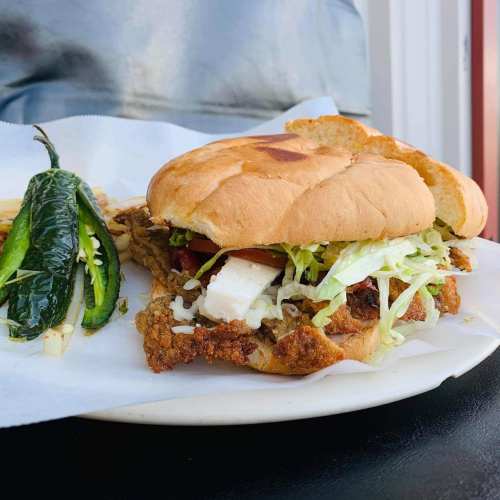 A crispy fried chicken sandwich with lettuce, tomato, and cheese, served with jalapeños and fries on the side.