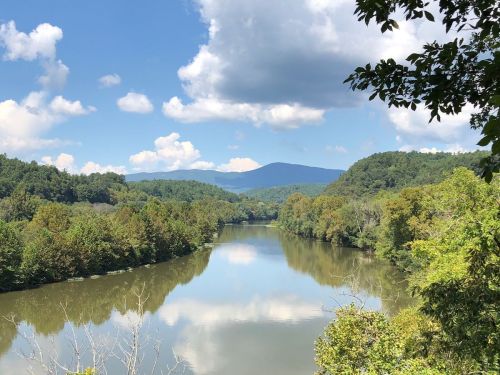 A serene river flows through lush green hills under a blue sky with fluffy clouds.