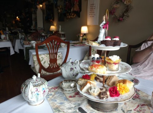 A tiered cake stand with assorted pastries and cupcakes, set on a floral tablecloth in a cozy tea room.