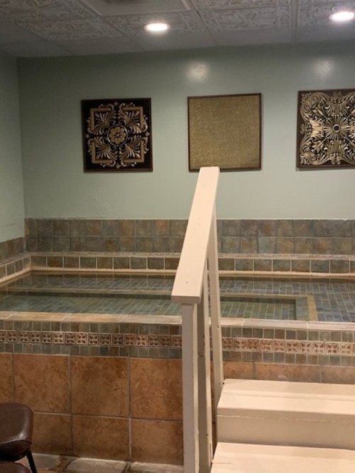 A serene indoor space featuring a tiled pool area, decorative wall art, and a staircase leading up.