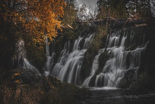 A serene waterfall cascades over rocks, surrounded by autumn foliage and a tranquil, darkened landscape.