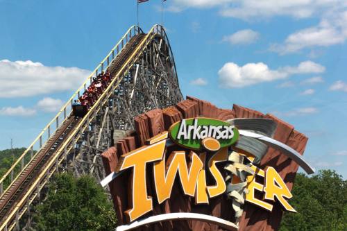 A wooden roller coaster named "Arkansas Twister" with riders ascending a steep track against a blue sky.