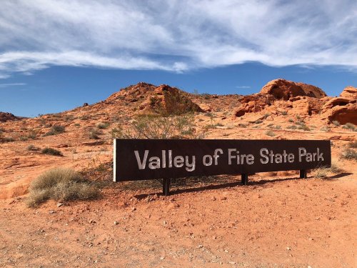 Sign for Valley of Fire State Park in a desert landscape with red rock formations and blue sky.