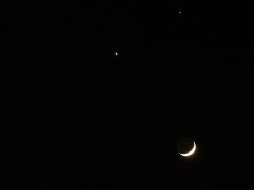 A crescent moon with two bright celestial bodies above it in a dark night sky.