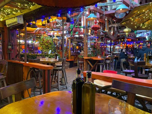 A vibrant restaurant interior with colorful lights, hanging decorations, and wooden tables set for dining.