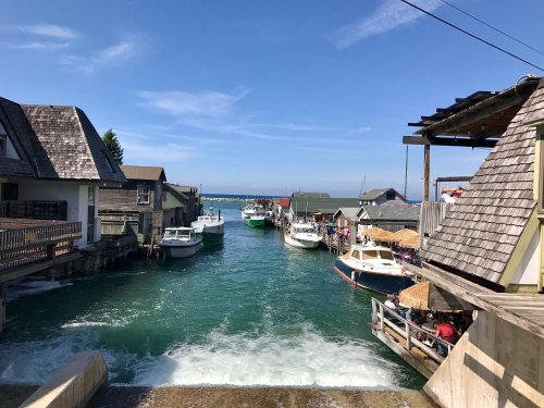 A scenic view of a harbor with boats lined up along the water, surrounded by quaint buildings under a clear blue sky.