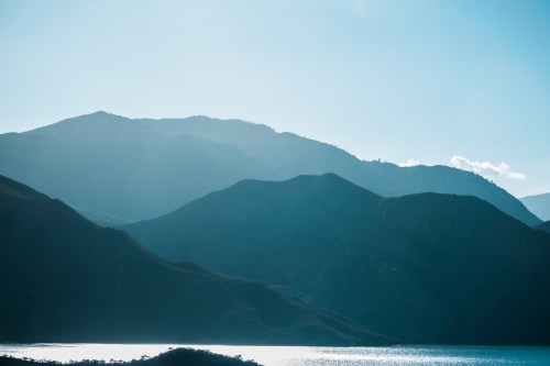Silhouetted mountains against a bright blue sky, reflecting on a calm body of water below.