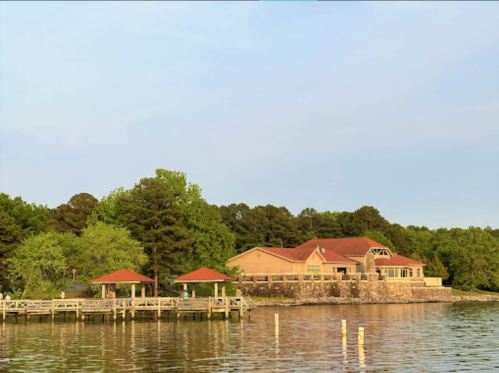 A lakeside building with a red-tiled roof, surrounded by trees and a wooden dock extending into the water.