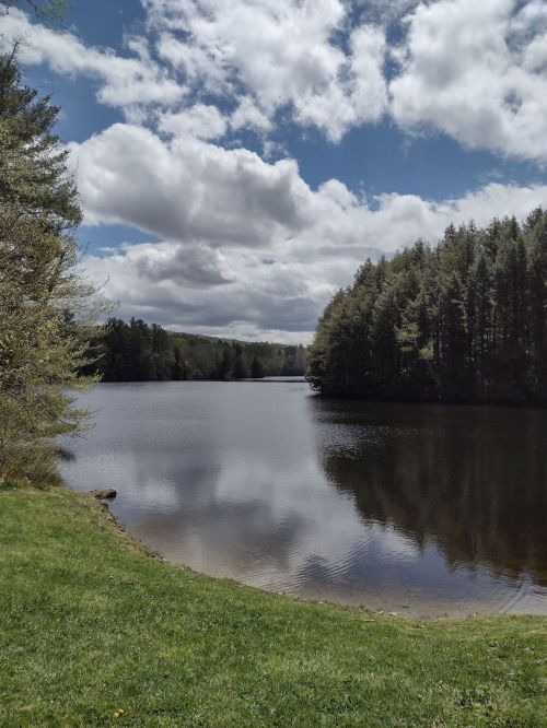 A serene lake surrounded by trees under a partly cloudy sky, reflecting the landscape on its calm surface.