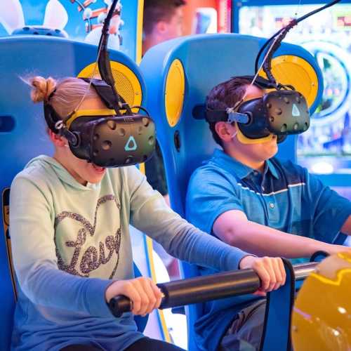 Two children wearing virtual reality headsets, excitedly gripping controls while experiencing a VR game.