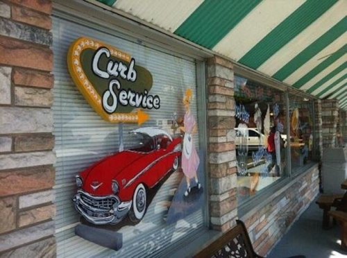 A retro diner window featuring a red car and a "Curb Service" sign, with colorful vintage decorations.