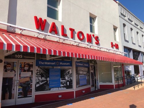 Exterior of Walton's 5-10 store, featuring red awning and signage, with displays about the Walmart Museum.