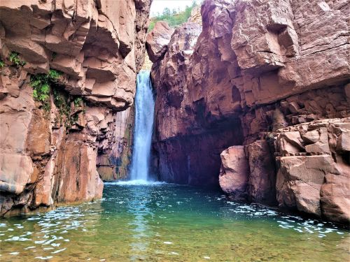 A stunning waterfall cascades between rocky cliffs into a serene, turquoise pool below.