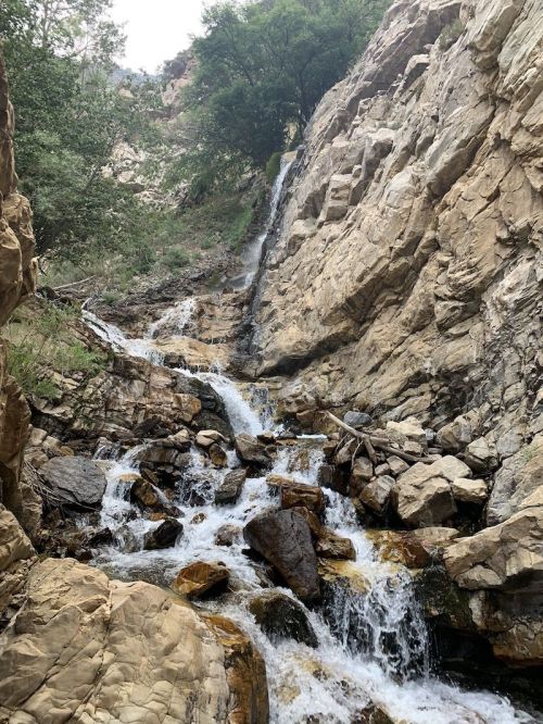 A cascading waterfall flows down rocky terrain, surrounded by lush greenery and steep cliffs.