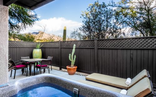 A serene outdoor space featuring a hot tub, lounge chairs, a dining table, and desert plants against a scenic backdrop.