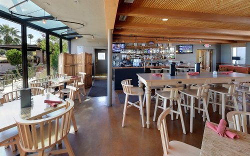 Interior of a modern restaurant featuring wooden tables, chairs, a bar, and large windows with outdoor views.