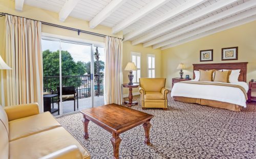 Spacious hotel room with a king bed, seating area, and balcony access, featuring warm colors and elegant decor.