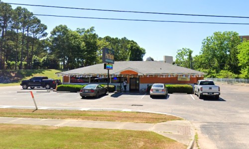 A casual restaurant with an orange exterior, surrounded by trees and parked cars in a spacious lot.