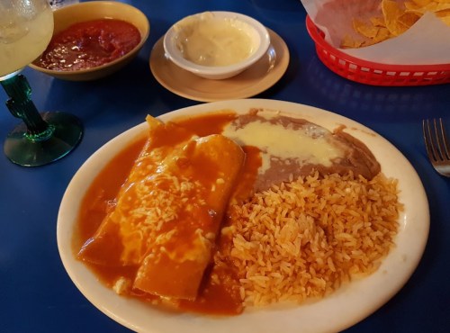 A plate of enchiladas with rice and refried beans, accompanied by salsa and sour cream on the side.