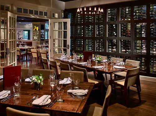 Elegant restaurant interior featuring wooden tables, glassware, and a wine wall in a warm, inviting atmosphere.