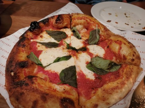 A freshly baked pizza topped with mozzarella cheese and fresh basil on a wooden table.