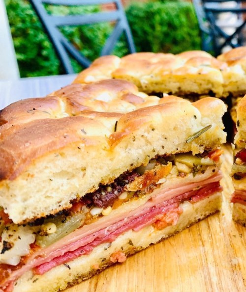 A close-up of a sliced sandwich with layers of meats, cheese, and vegetables on a golden, fluffy bread.