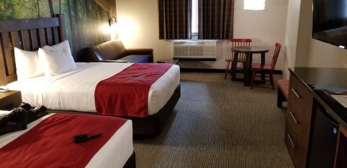 A hotel room with two beds, a seating area, a table, and a TV, featuring warm colors and a cozy atmosphere.