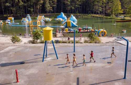 Children play in a splash pad area near a lake with inflatable water attractions in the background.