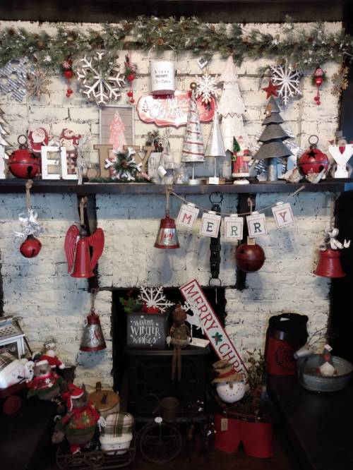 A festive display of Christmas decorations, including snowflakes, trees, and cheerful signs, on a rustic shelf.