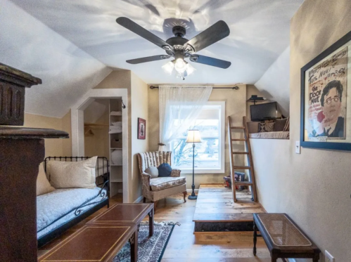 Cozy living space with a ceiling fan, a daybed, armchair, wooden ladder, and a window letting in natural light.