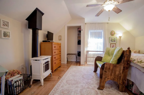 Cozy bedroom with a wooden bed, dresser, small TV, and a decorative stove, featuring soft lighting and a rug.