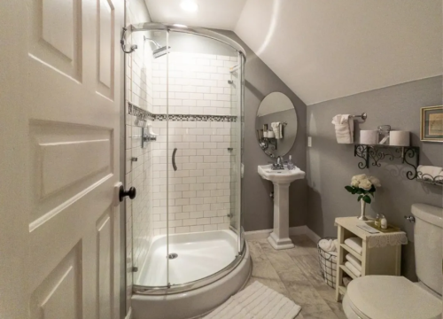 A cozy bathroom featuring a glass shower, pedestal sink, and decorative shelving with towels and flowers.