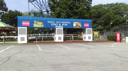 Entrance sign for York's Wild Kingdom Zoo & Fun Park, featuring a Coca-Cola logo and surrounding greenery.