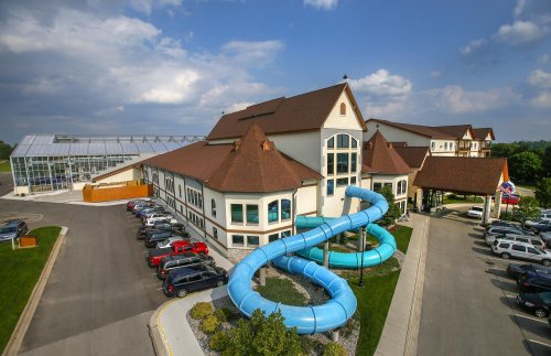 A large building with a blue water slide curving around it, surrounded by parked cars and a clear sky.