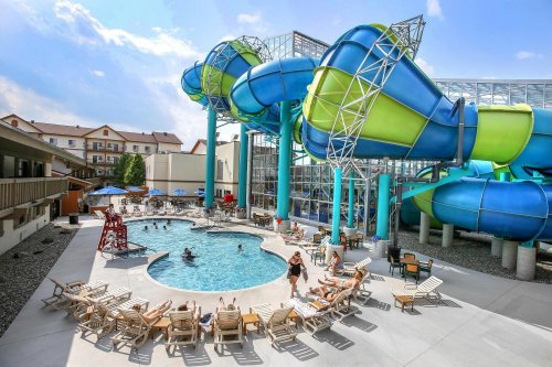 A vibrant water park featuring large water slides, a pool, and sun loungers, with people enjoying the sunny day.