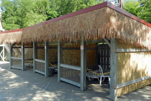 A shaded outdoor area with thatched roofs and lounge chairs, surrounded by bamboo fencing.