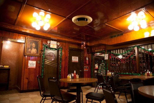 Cozy diner interior with wooden walls, round tables, and festive decorations, featuring vintage lighting and a portrait.