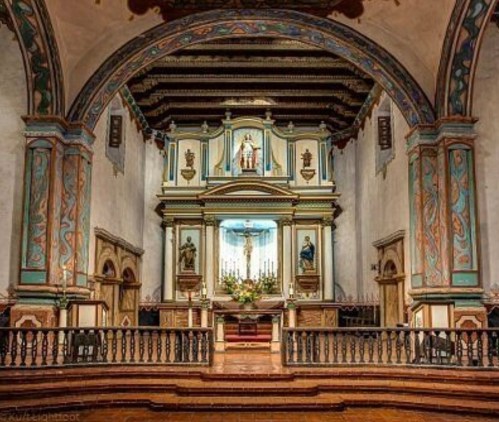 Interior of a historic church featuring ornate decorations, an altar, and colorful murals on the walls.