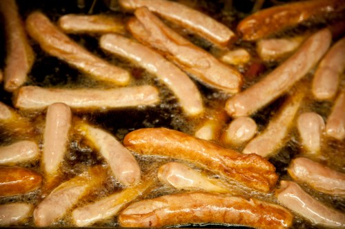 A close-up of various sausages sizzling in a frying pan, surrounded by bubbling oil.