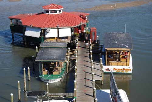 Aerial view of two boats docked at a waterfront restaurant with a red roof and wooden pier.