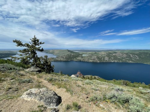 A scenic view of a lake surrounded by hills and trees under a partly cloudy sky.