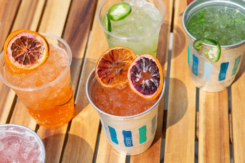 Colorful drinks with ice and garnishes, arranged on a wooden table.