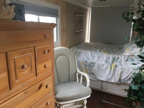 Cozy bedroom with a wooden dresser, rocking chair, and a bed adorned with floral bedding near a window.