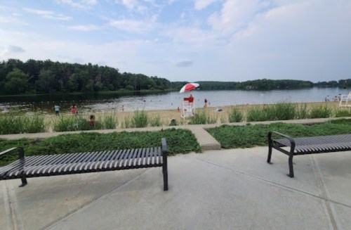 A serene beach scene with a lifeguard station, benches, and people enjoying the water under a cloudy sky.