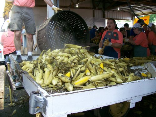 A man pours corn husks from a basket onto a table, while others work in a busy market setting.