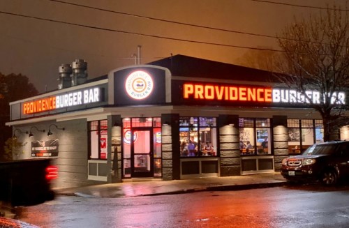 A brightly lit burger restaurant at night, featuring a sign that reads "Providence Burger Bar."