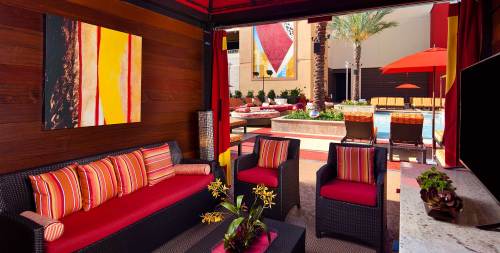 Cozy outdoor lounge area with red and orange decor, overlooking a pool and palm trees.