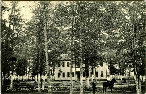 A historic black-and-white photo of a school campus with trees, featuring a boy and a horse in front of a building.